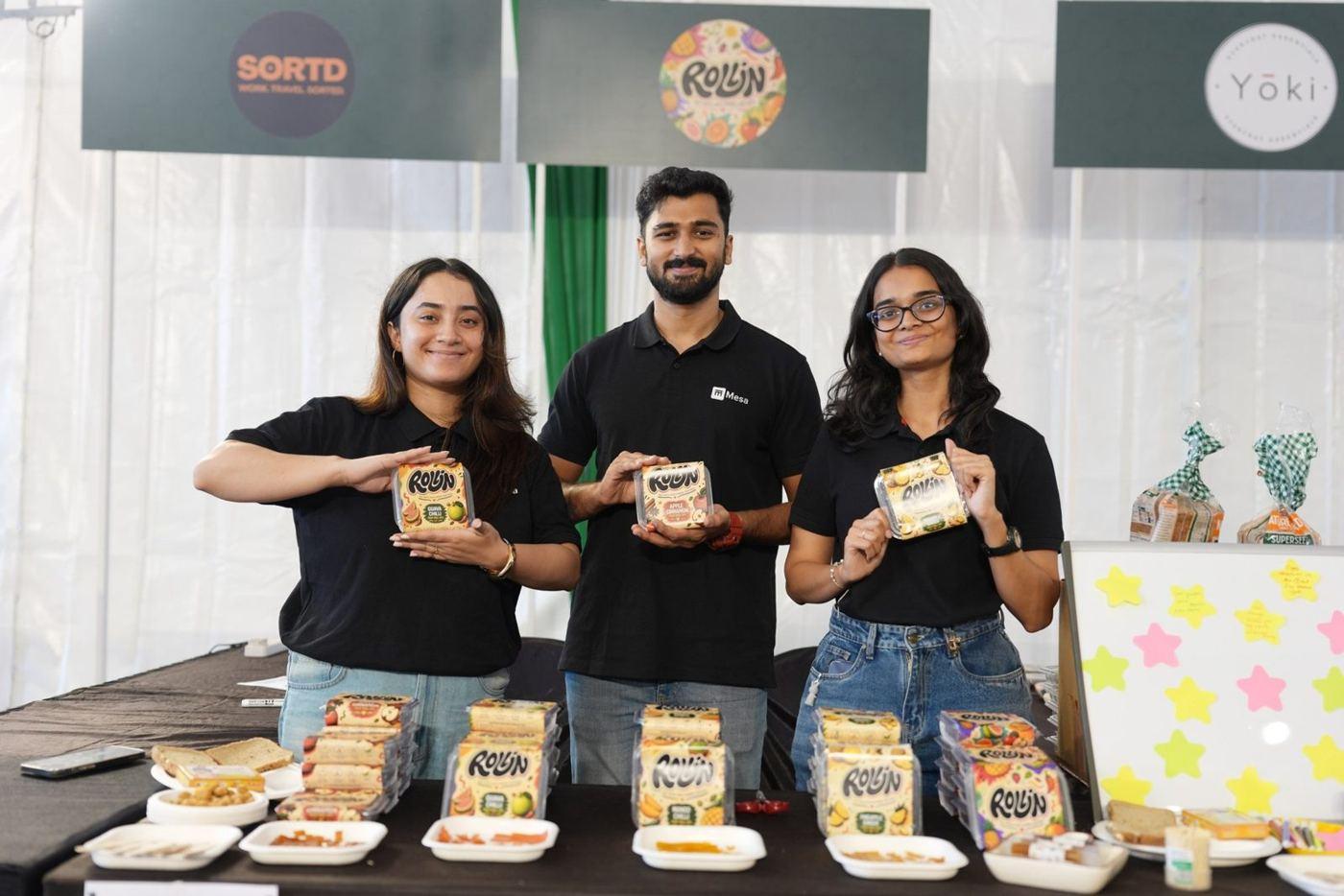 Three student founders presenting their packaged food products at a market stall